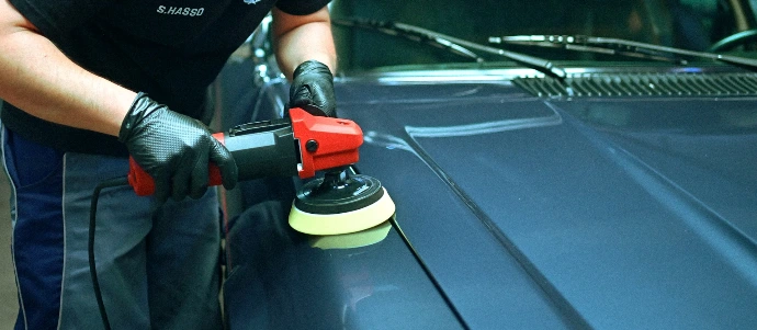 Person polishing a blue car's hood with an orbital buffer.